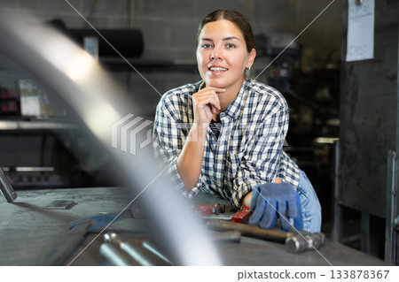 Smiling young female worker posing in metalworking workshop Smiling young female worker posing in metalworking workshop 133878367