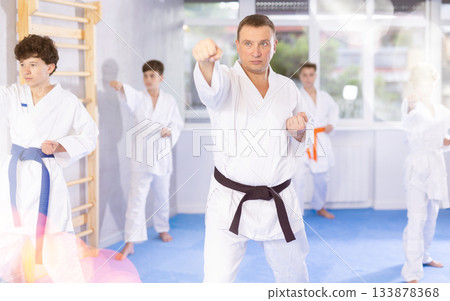 Karate kids in kimono performing kata moves with their teacher in foreground in gym during group training 133878368