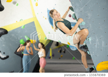Woman climbs artificial wall bouldering, working out in gym 133878369