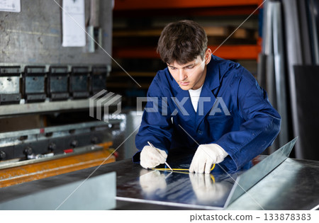 Guy measuring sheet of metal with tape measure Guy measuring sheet of metal with tape measure 133878383