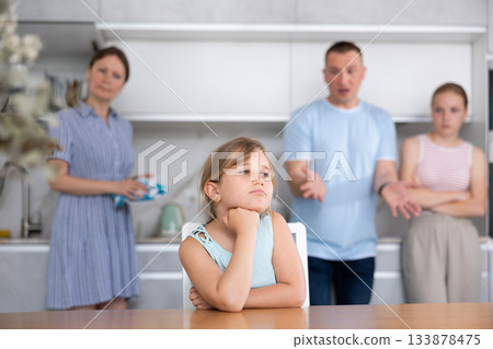 At home kitchen parents scold sitting child for bad behavior, mother clean dish in background 133878475