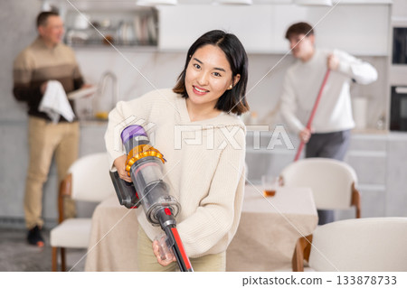 Girl vacuuming floor while his relatives help tidy up room Girl vacuuming floor while his relatives help tidy up room 133878733