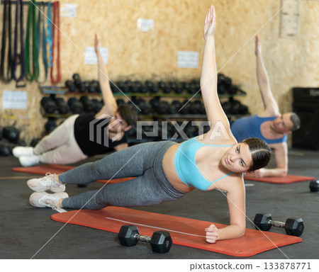 Young girl holding side plank pose during group training Young girl holding side plank pose during group training 133878771