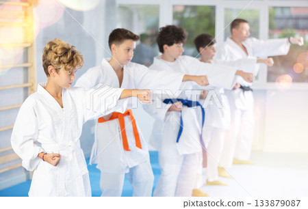 Preteen attendee of karate classes practicing kata standing in row with others 133879087