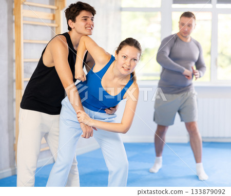 Self-defense class - a woman learns to fight back an attacking man under the guidance of trainer Self-defense class - a woman learns to fight back an attacking man under the guidance of trainer 133879092