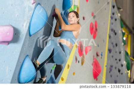 Woman exercising on wall in climbing gym during bouldering training Woman exercising on wall in climbing gym during bouldering training 133879118