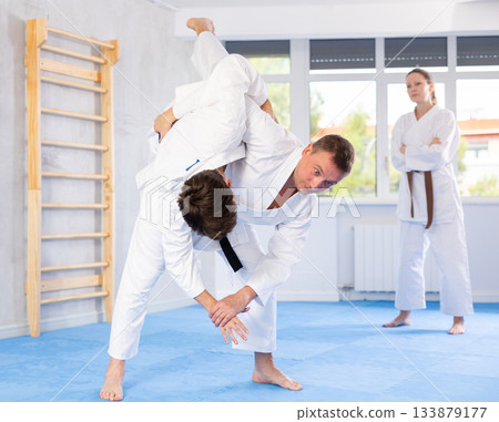 Two males practicing judo together on sports mats under the guidance of trainer 133879177