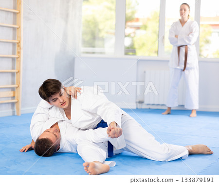 Male athletes in pair conduct training battle in oriental fighting technique under guidance of coach 133879191
