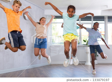 Group of positive juvenile boys and girls jumping cheerfully in dancehall 133879197