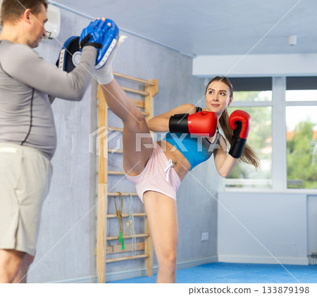 Young girl training boxing kicks on punch mitts held by male instructor 133879198