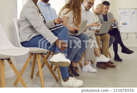 Group of young business people sitting on chairs in row with resumes and laptops and talking. 133879358