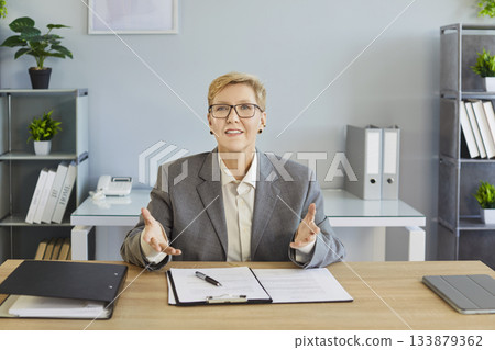 Smiling business coach explaining with open hands during online meeting in office Smiling business coach explaining with open hands during online meeting in office 133879362