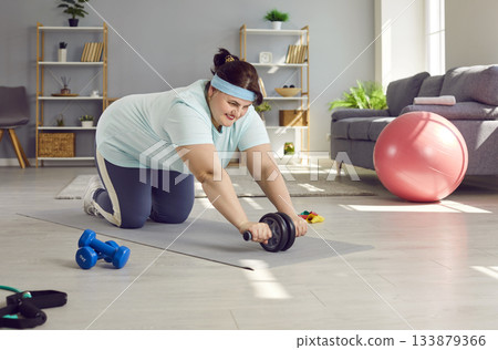 Happy, plus size woman doing exercise with ab roller during her fitness workout at home Happy, plus size woman doing exercise with ab roller during her fitness workout at home 133879366
