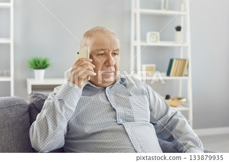Senior Man Having A Serious Phone Conversation On Sofa In Living Room Senior Man Having A Serious Phone Conversation On Sofa In Living Room 133879935
