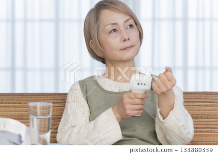 Senior woman measuring her temperature with a thermometer in the living room 133880339