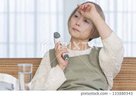 一位老婦人在客廳用體溫計測量體溫 133880343