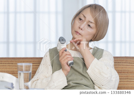 一位老婦人在客廳用體溫計測量體溫 一位老婦人在客廳用體溫計測量體溫 133880346