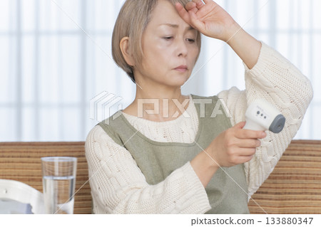 一位老婦人在客廳用體溫計測量體溫 133880347