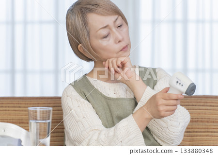 一位老婦人在客廳用體溫計測量體溫 133880348