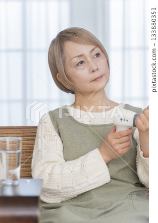 Senior woman measuring her temperature with a thermometer in the living room Senior woman measuring her temperature with a thermometer in the living room 133880351