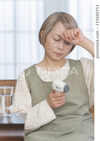 一位老婦人在客廳用體溫計測量體溫 133880353