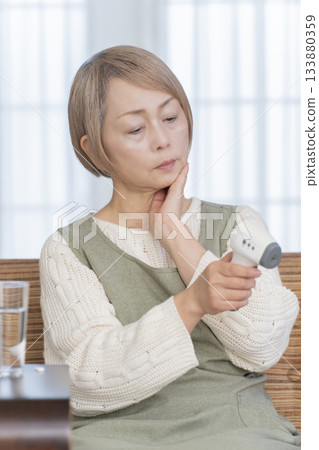 一位老婦人在客廳用體溫計測量體溫 133880359