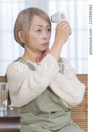 一位老婦人在客廳用體溫計測量體溫 一位老婦人在客廳用體溫計測量體溫 133880362
