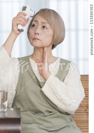 Senior woman measuring her temperature with a thermometer in the living room 133880363