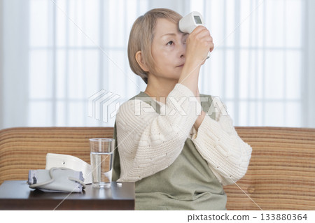 一位老婦人在客廳用體溫計測量體溫 133880364