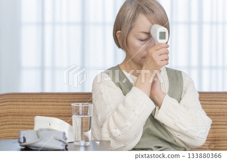 Senior woman measuring her temperature with a thermometer in the living room 133880366