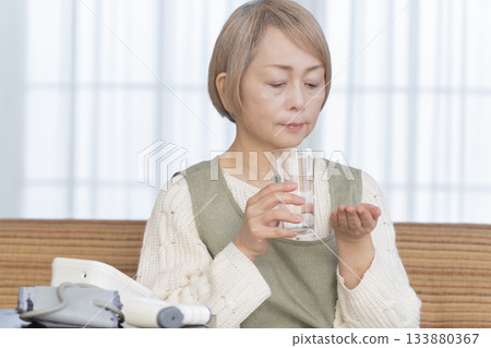 一位老婦人在客廳用體溫計測量體溫 一位老婦人在客廳用體溫計測量體溫 133880367
