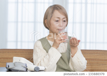 Senior woman measuring her temperature with a thermometer in the living room 133880370