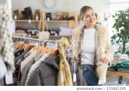 Beautiful woman standing in clothing shop and trying new warm fur coat for autumn-winter season Beautiful woman standing in clothing shop and trying new warm fur coat for autumn-winter season 133881195