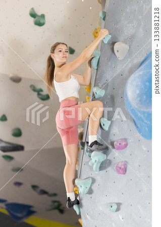 Girl climbs artificial wall bouldering, working out in gym Girl climbs artificial wall bouldering, working out in gym 133881218