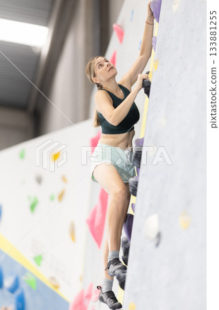 Woman training at bouldering gym without special climbing equipment 133881255