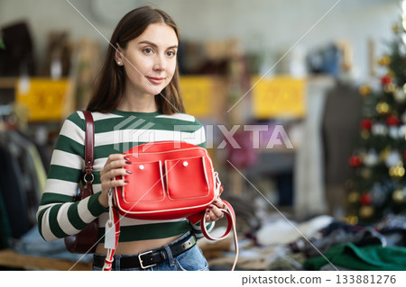 Positive young woman choosing handbag in clothing store 133881276