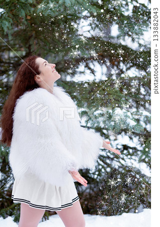 Woman in a white fur coat in the snowy winter forest. Woman in a white fur coat in the snowy winter forest. 133882043