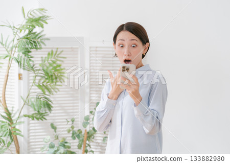 一位女士一臉驚訝地看著她的智慧型手機。 一位女士一臉驚訝地看著她的智慧型手機。 133882980