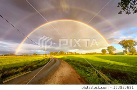A vibrant double rainbow arches over a scenic country road, creating a mesmerizing view 133883681