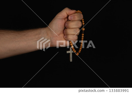 Hand holding rosary beads with a cross against a dark background 133883991