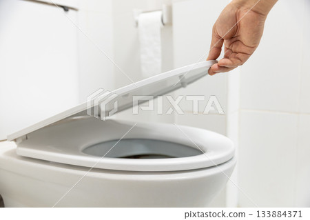 Close up hand is opening the lid of a toilet seat. 133884371