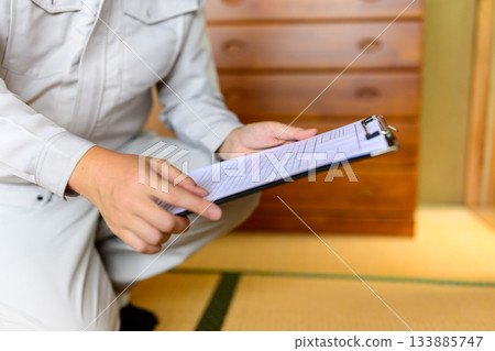 A Japanese man in work clothes sits in a Japanese-style room and checks documents (close-up of hands) 133885747