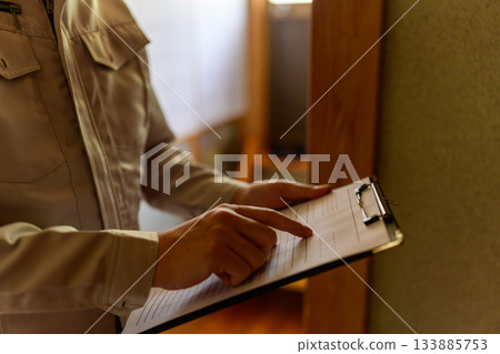 A man in work clothes points to a document on a clipboard and checks it 133885753