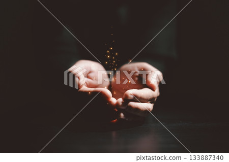 Hands holding glowing light, symbolizing hope, healing, faith, inspiration, spiritual energy, new beginning, miracle, inner strength and positive transformation from darkness to light. 133887340