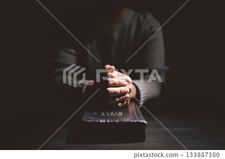 Hands clasped in prayer over the Holy Bible, symbolizing faith, devotion, Christianity, hope and spiritual strength through God Word, worship, meditation and encouragement. 133887380