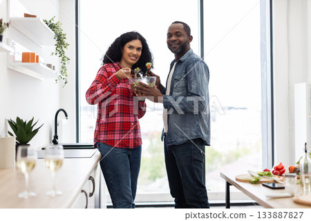 A smiling couple prepares a salad together in a bright, modern kitchen, enjoying a healthy meal. 133887827