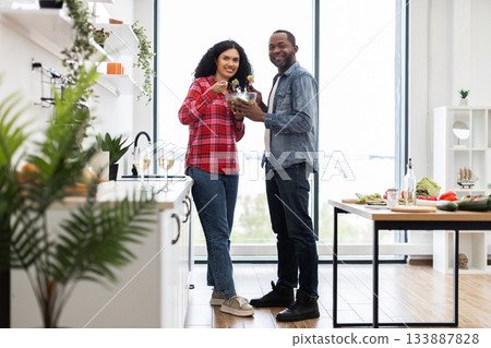A smiling couple prepares a salad together in a bright, modern kitchen, enjoying a healthy meal. 133887828