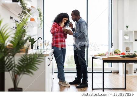 A couple enjoys a healthy meal together in a bright, modern kitchen setting, sharing a salad. 133887829