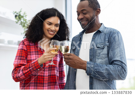 A smiling couple clinking glasses of white wine, celebrating together in a bright setting. 133887830