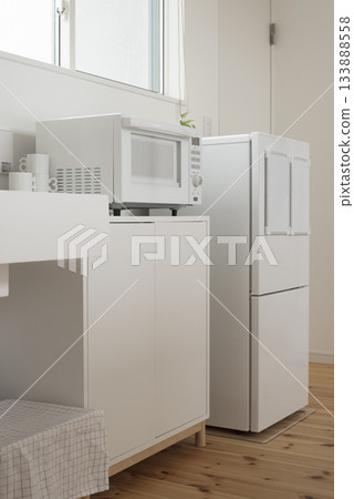 A clean white mini kitchen with a refrigerator and microwave 133888558